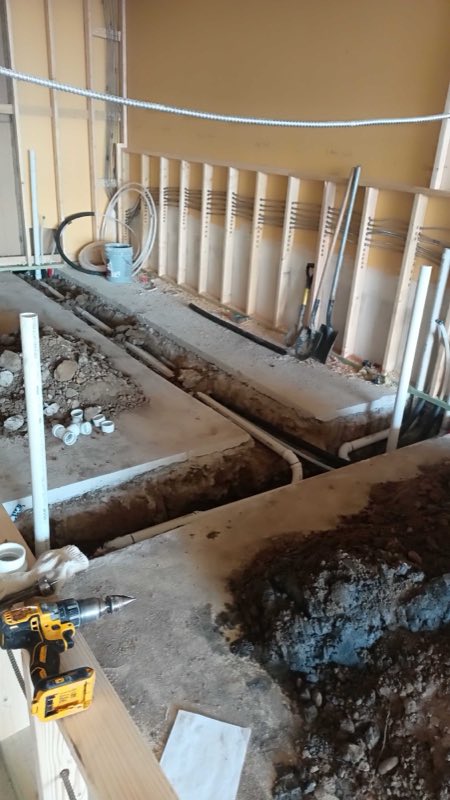 Trenches cut through a concrete slab floor with new drain pipe being run for an under-slab repipe.